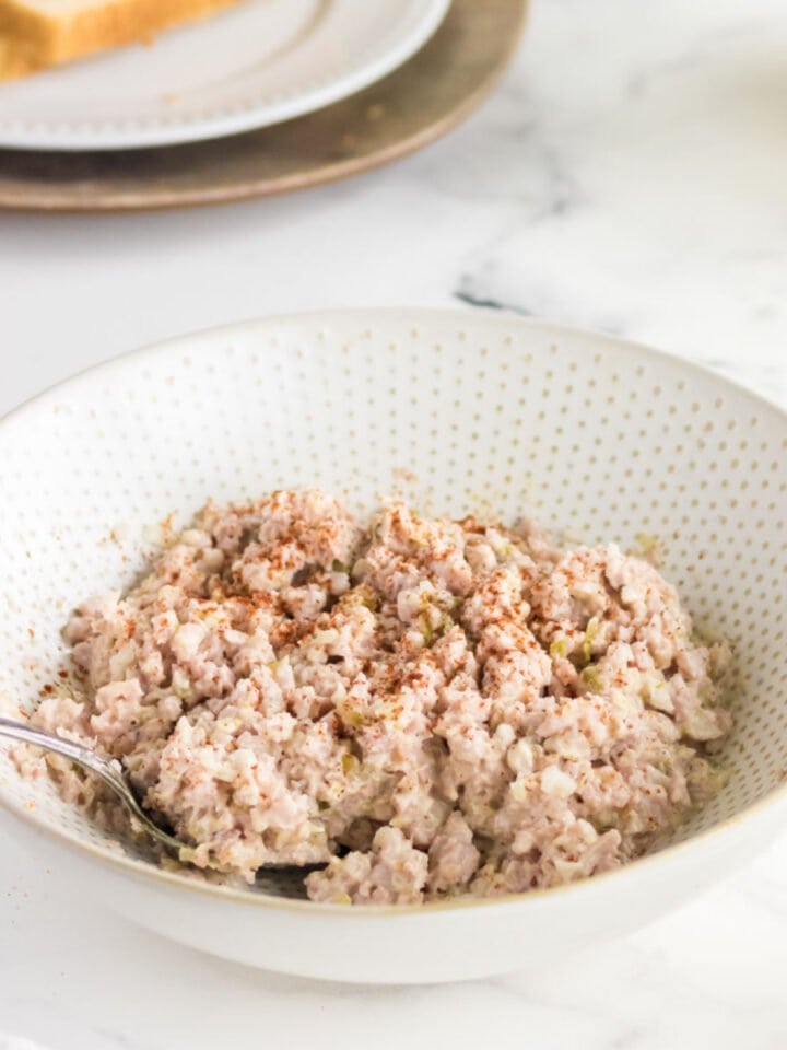 A bowl of ham salad with a spoon in it.