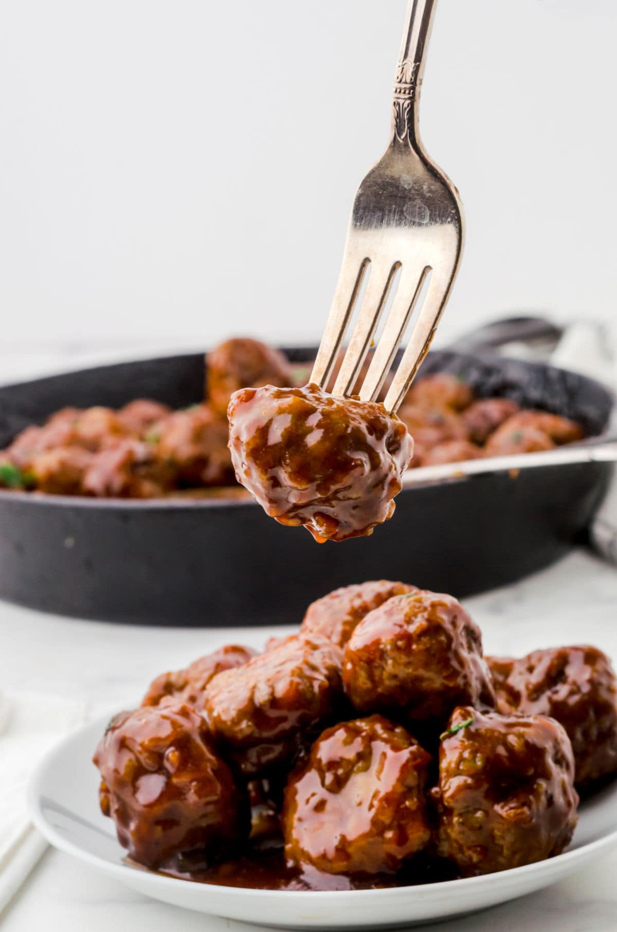 A meatball on a fork dripping with sauce.
