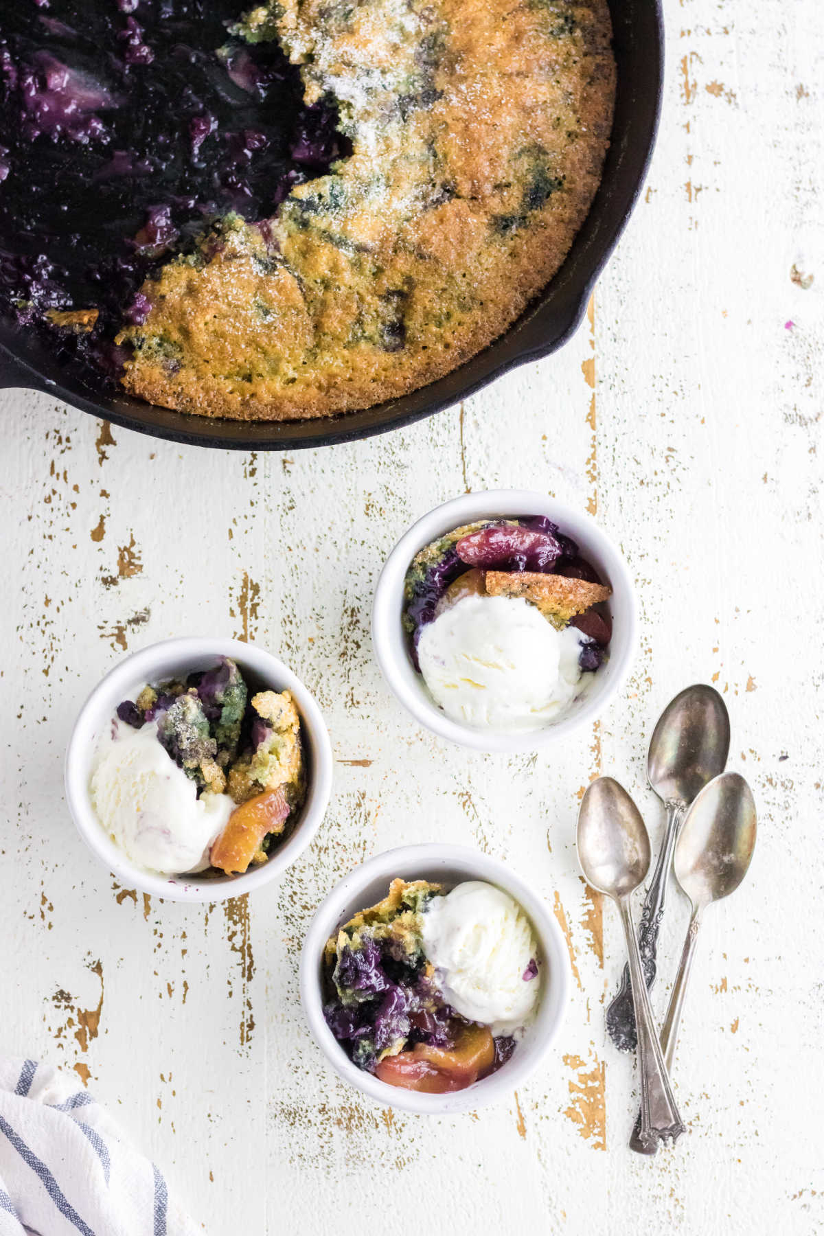 A skillet of blueberry peach cobbler being served.