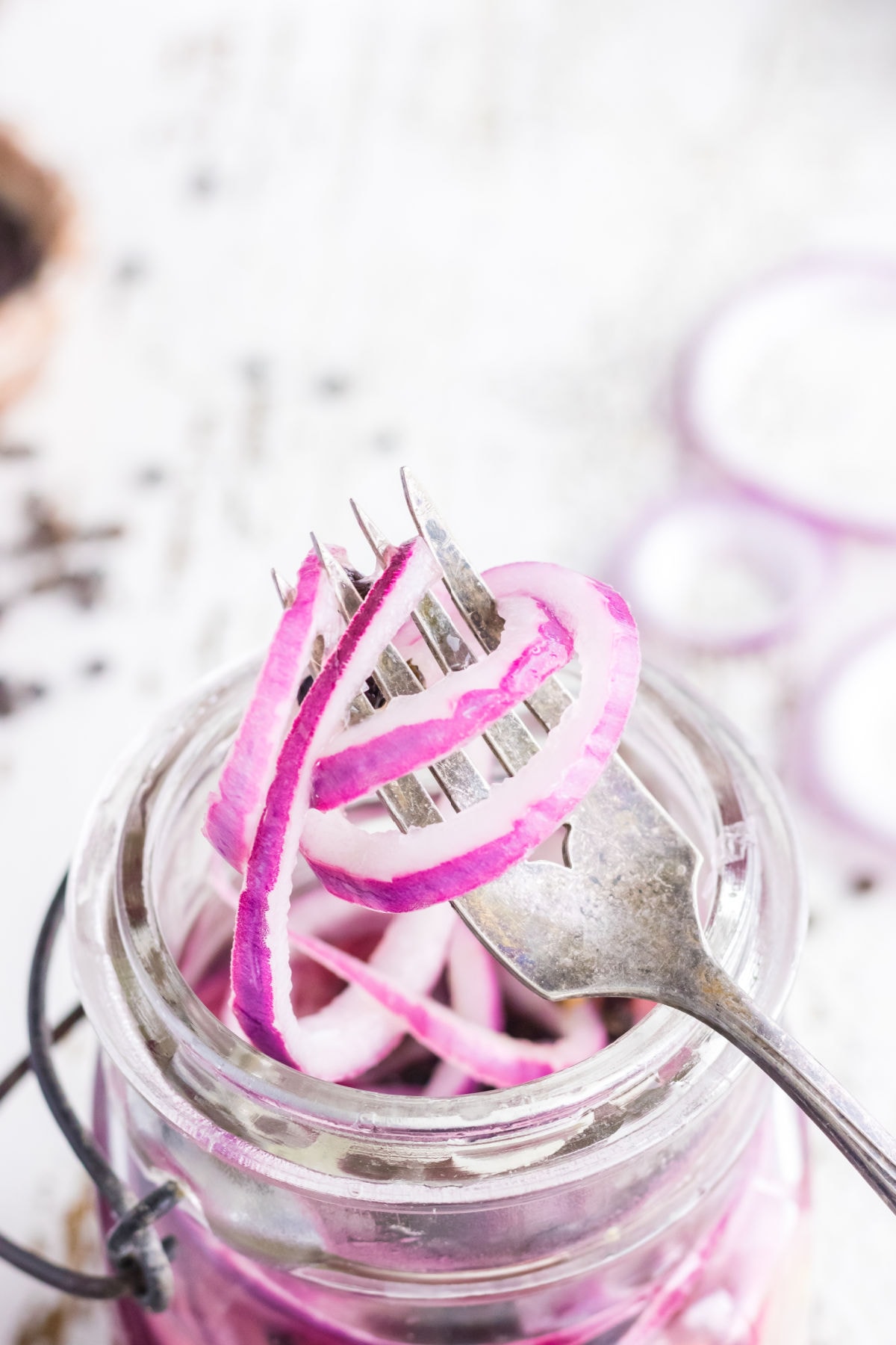 Pickled onion rings on a fork being removed from the jar.