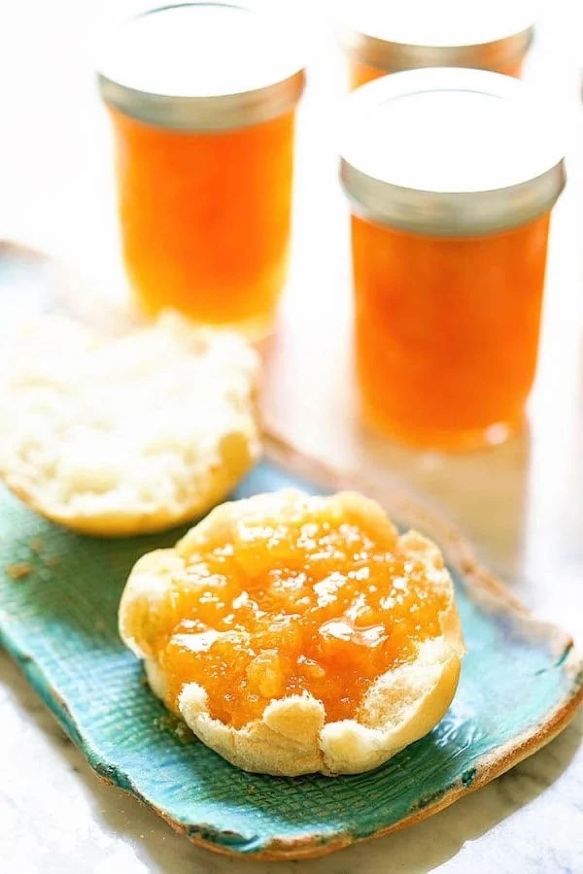 Apricot Jam spooned on a toasted English muffin on a green plate.