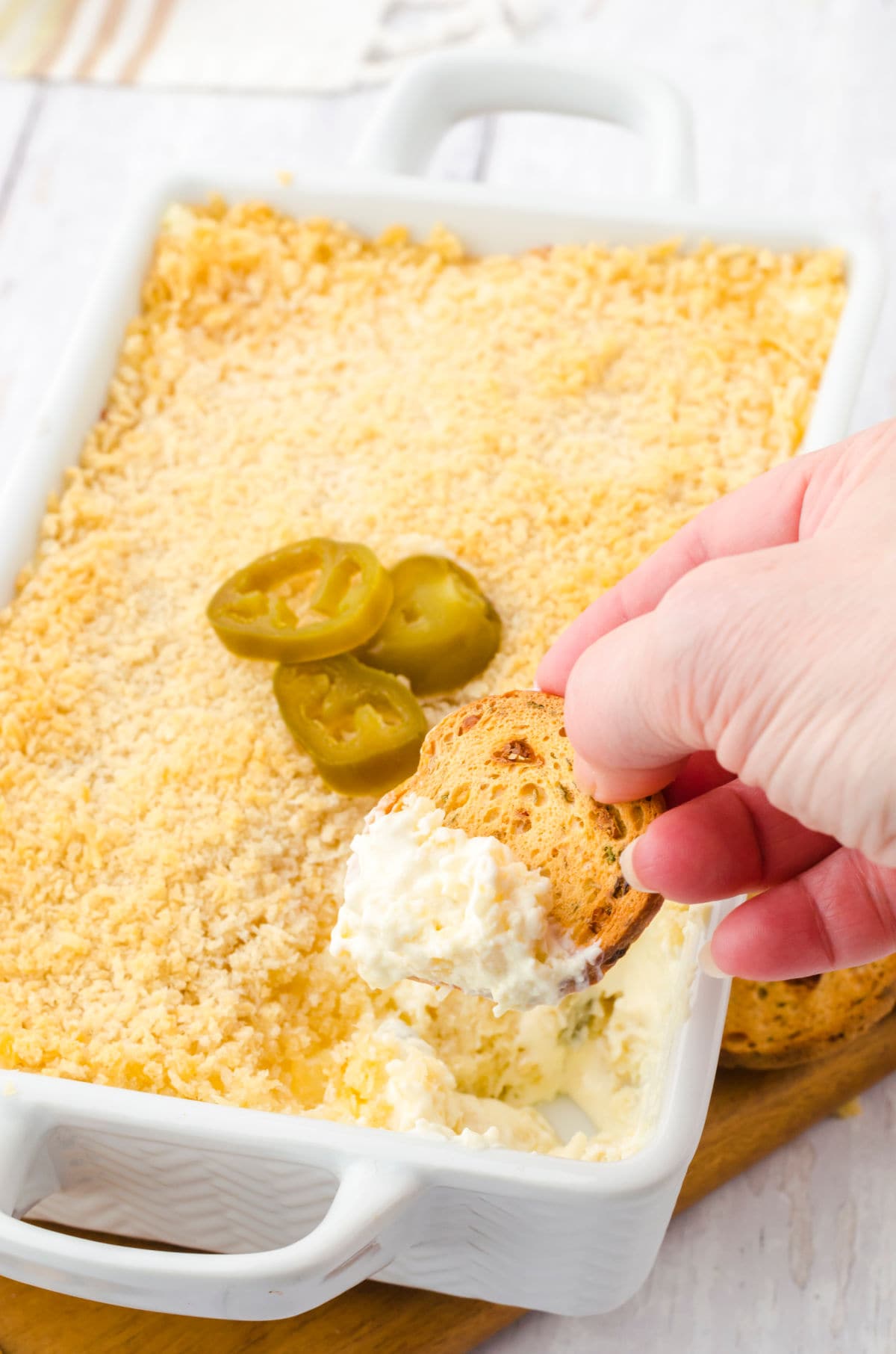 A hand dipping a cracker into the jalapeno popper dip.