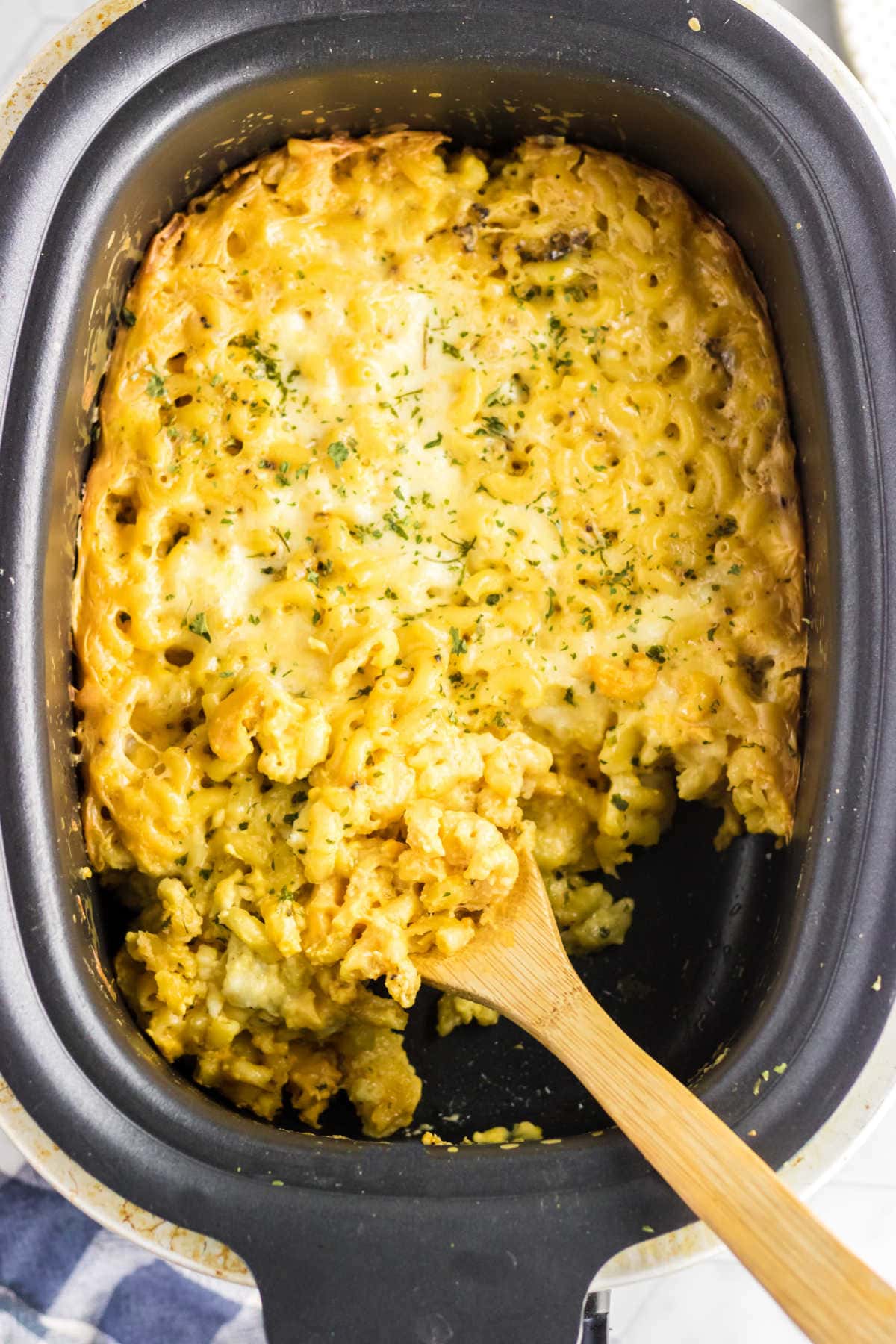 Macaroni and cheese in the crockpot with a wooden spoon.