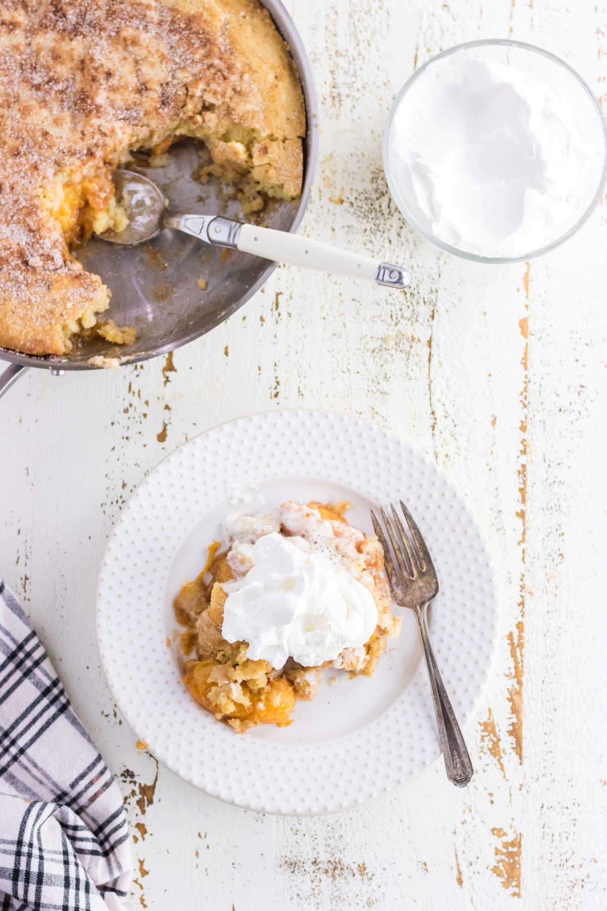 A serving of peach cobbler on a white plate with a spoonful of whipped cream on top.