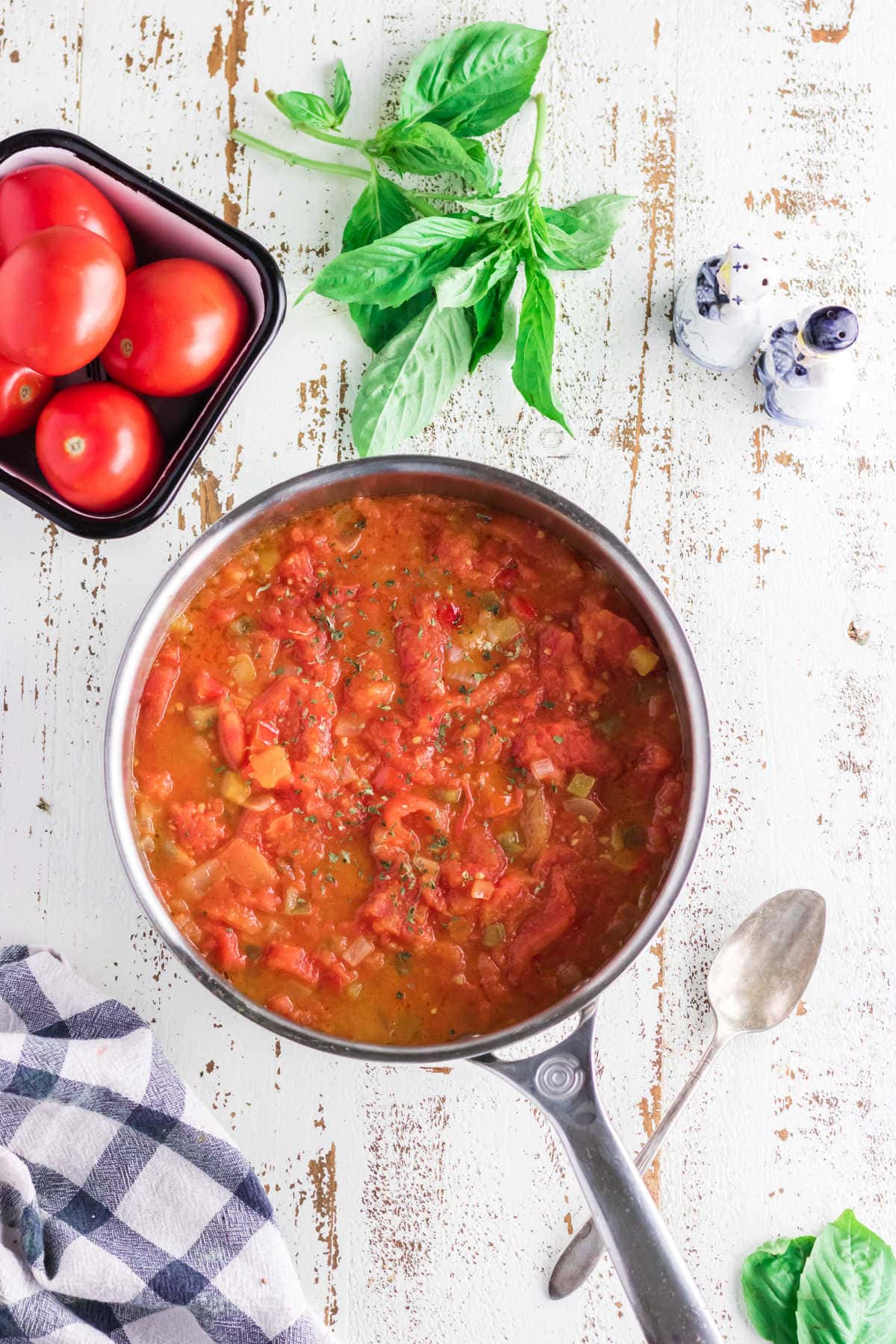 A white wooden table top with a pan of stewed tomatoes on it.