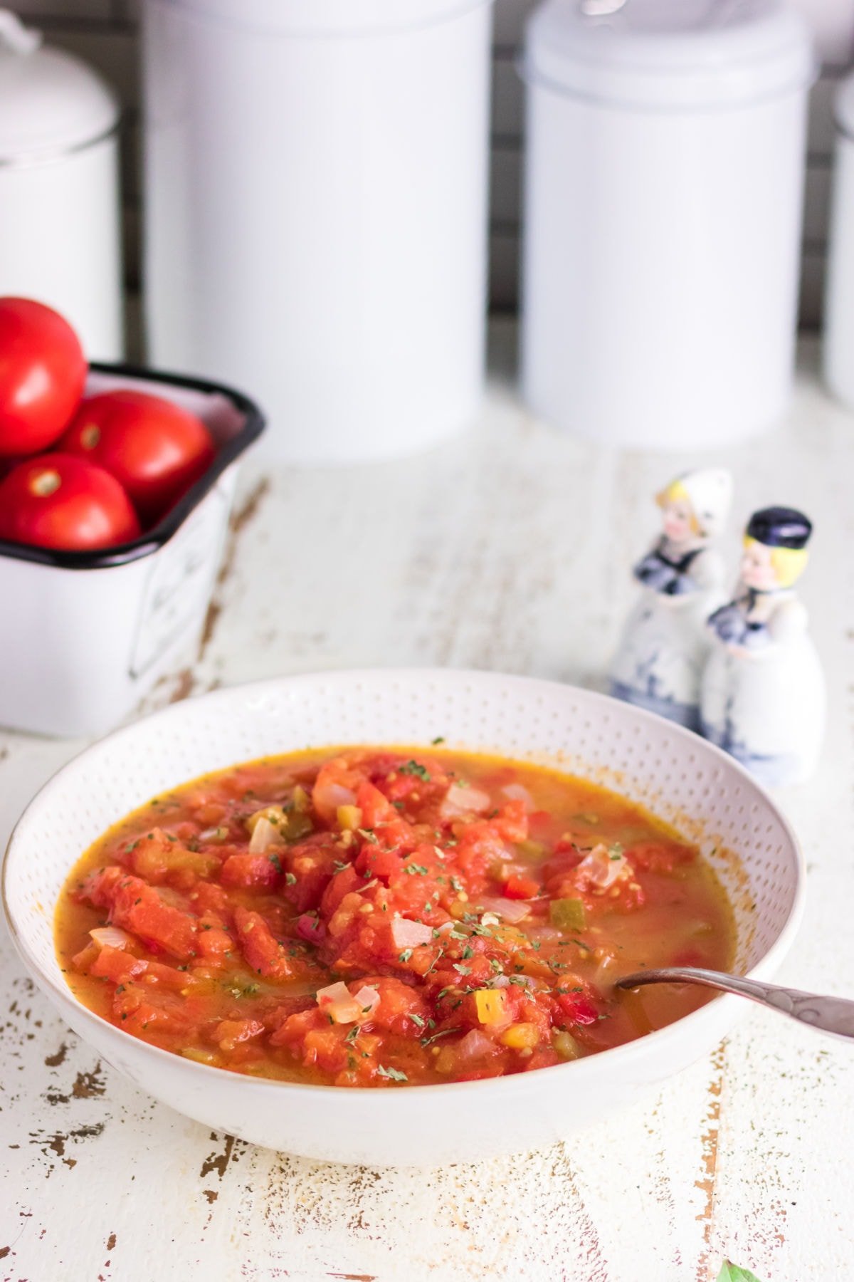 A bowl of stewed tomatoes on a white wooden counter.