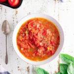 Overhead view of stewed tomatoes in a white bowl with a spoon next to it.