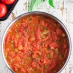 A pan of stewed tomatoes on a white wooden table with text overlay for Pinterest.