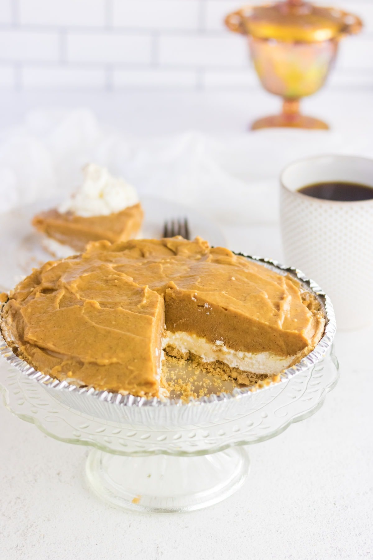 A pumpkin pie with a slice removed to show the cream cheese and pumpkin layers.