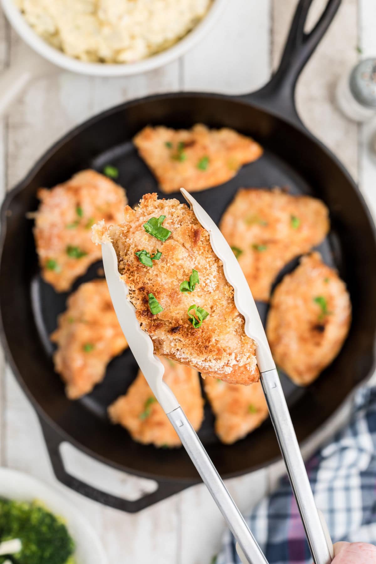 Tongs lifting a piece of chicken from the pan.