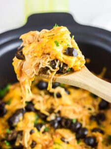 A spoonful of enchilada casserole being removed from the slow cooker.