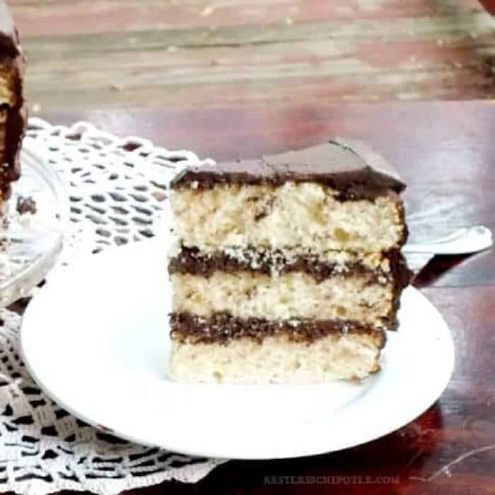 A slice of vanilla cake with chocolate frosting and filling.