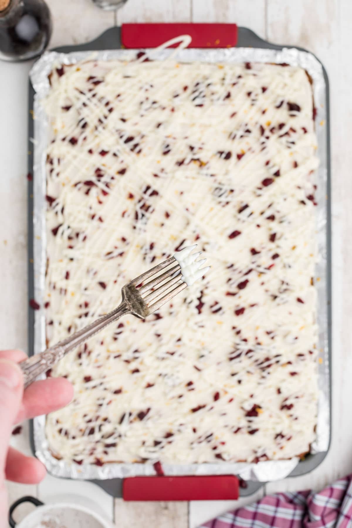 Overhead shot of cranberry bliss bars with fork over them drizzling white chocolate over them.