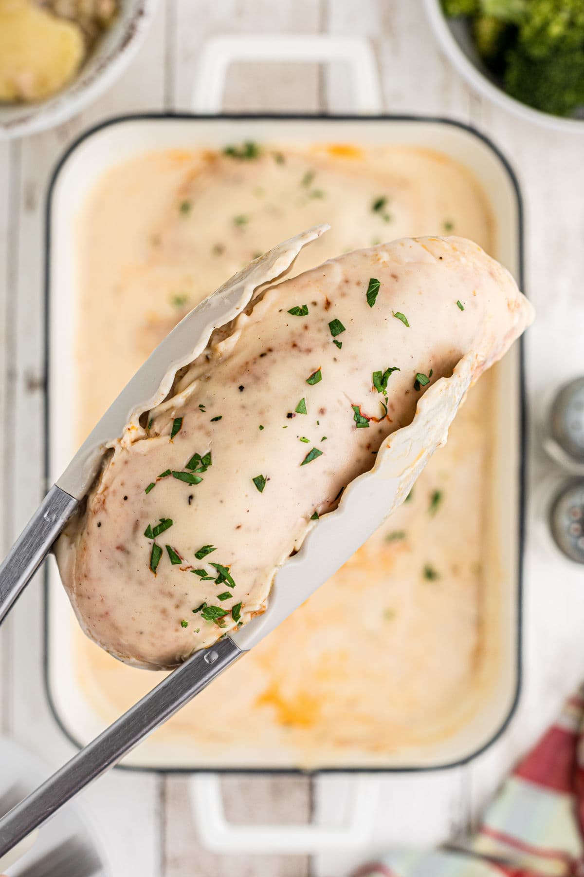 Tongs holding up a piece of finished chicken.