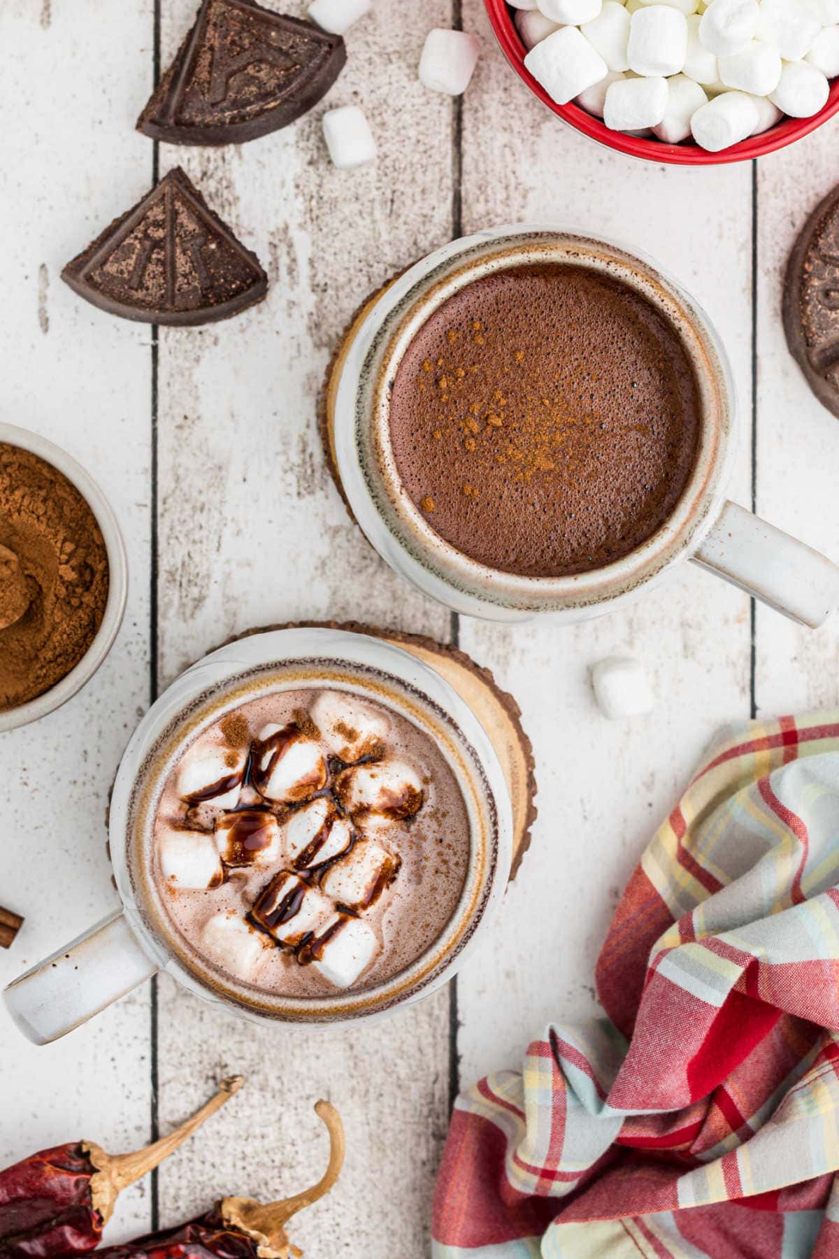 Overhead view of two cups of hot chocolate with ingredients on the table nearby.