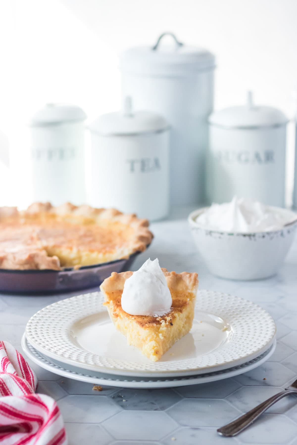 Buttermilk pie on a white plate with a dollop of whip cream.