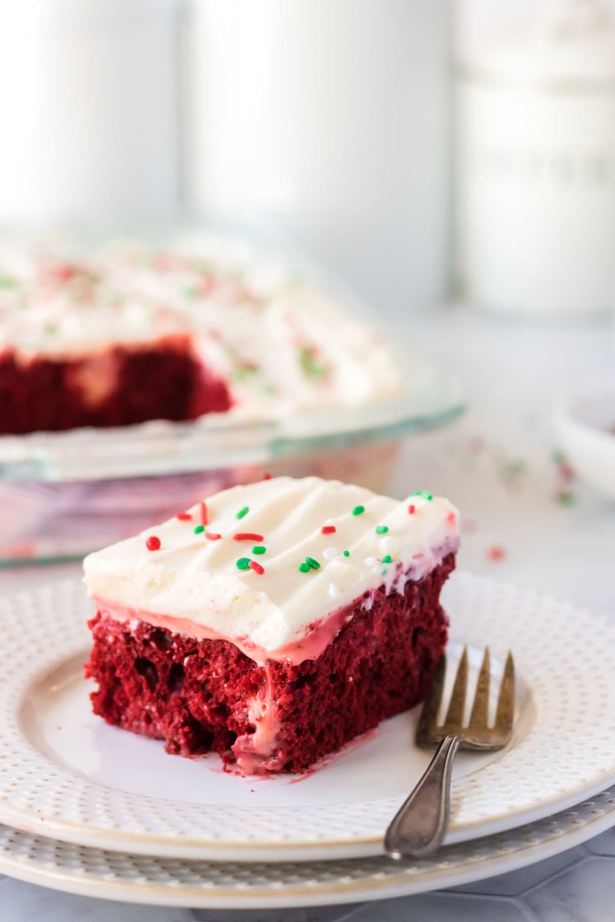 A piece of red velvet poke cake on a white plate with a fork.