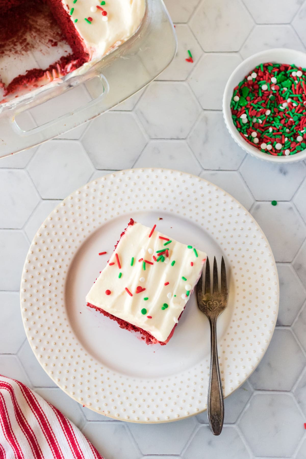 A piece of red velvet poke cake on a white plate with a fork next to it.