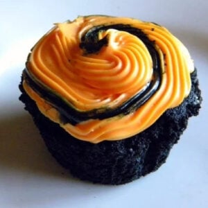 A closeup of a black cupcake with orange frosting.