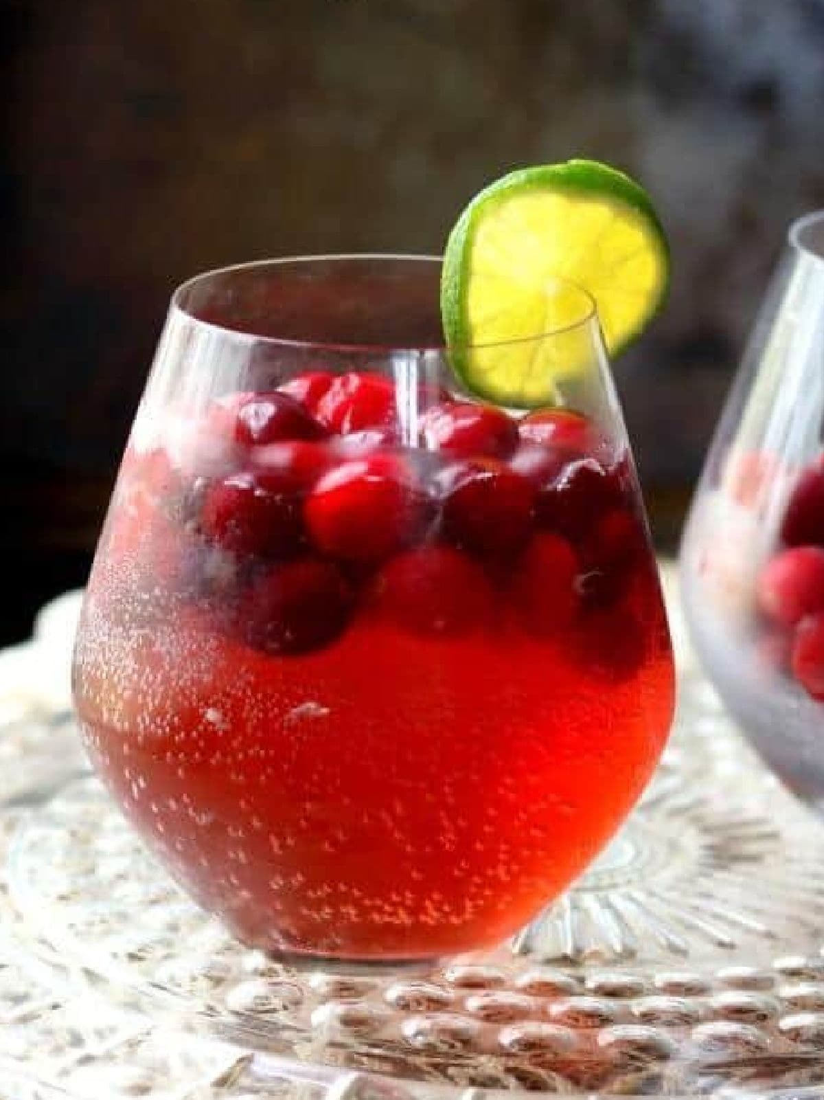 A bright red cocktail with frozen cranberries floating in it.