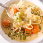 Closeup of a spoonful of creamy chicken noodle soup.