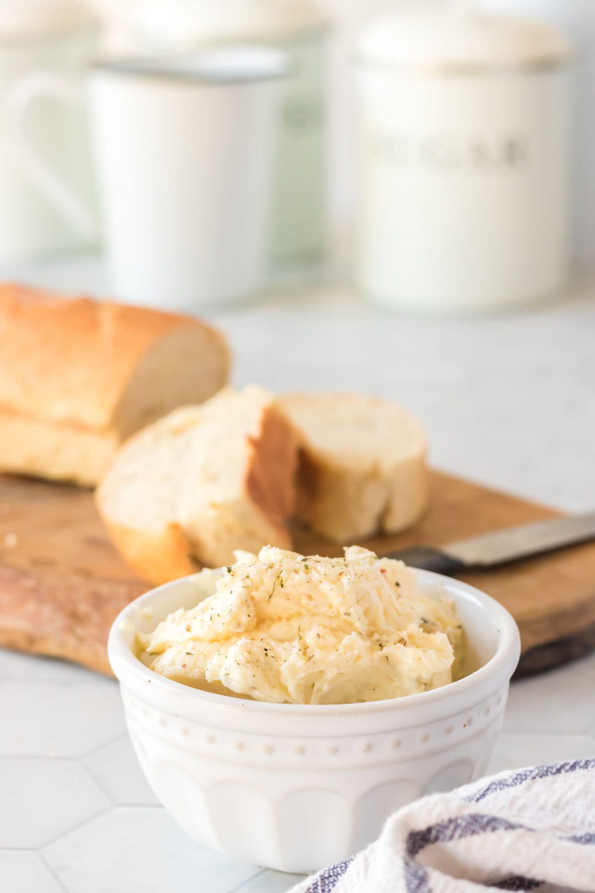 Garlic butter in a white bowl with bread and a knife behind it.