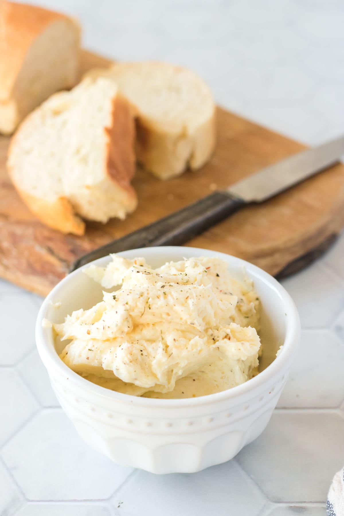 Garlic butter in a white bowl with bread behind it.