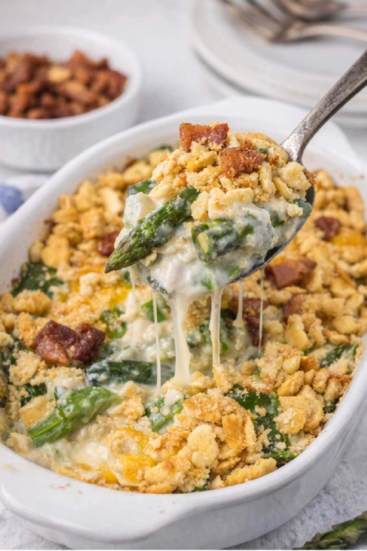 Asparagus casserole in a white baking dish with a spoon being lifted from the dish.