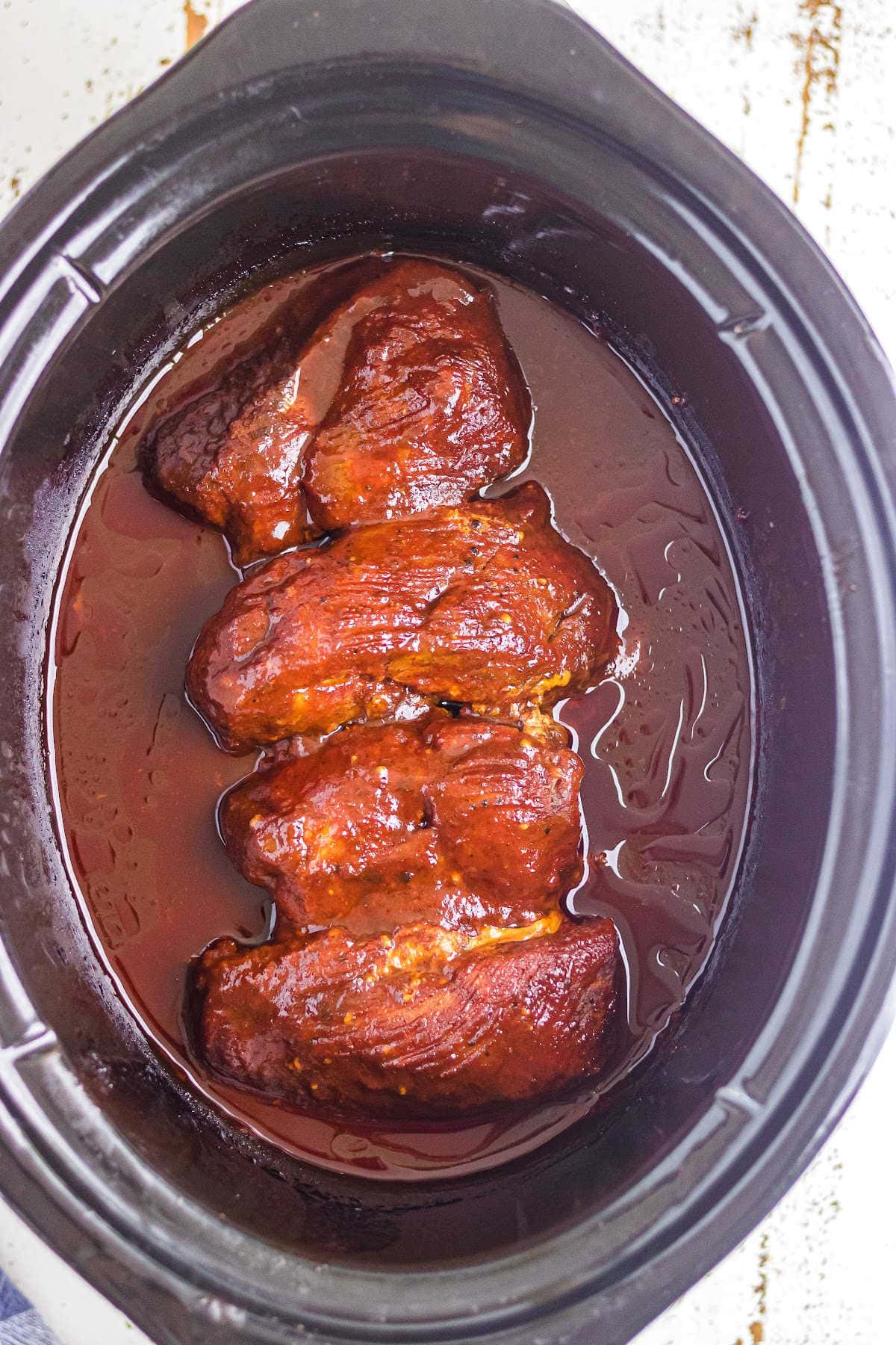 Overhead view of pork ribs in a tangy sauce in the slow cooker.
