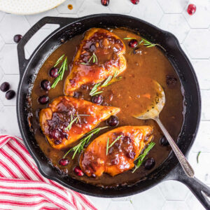 A skillet of cranberry chicken with a serving spoon in it.