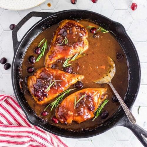 A skillet of cranberry chicken with a serving spoon in it.