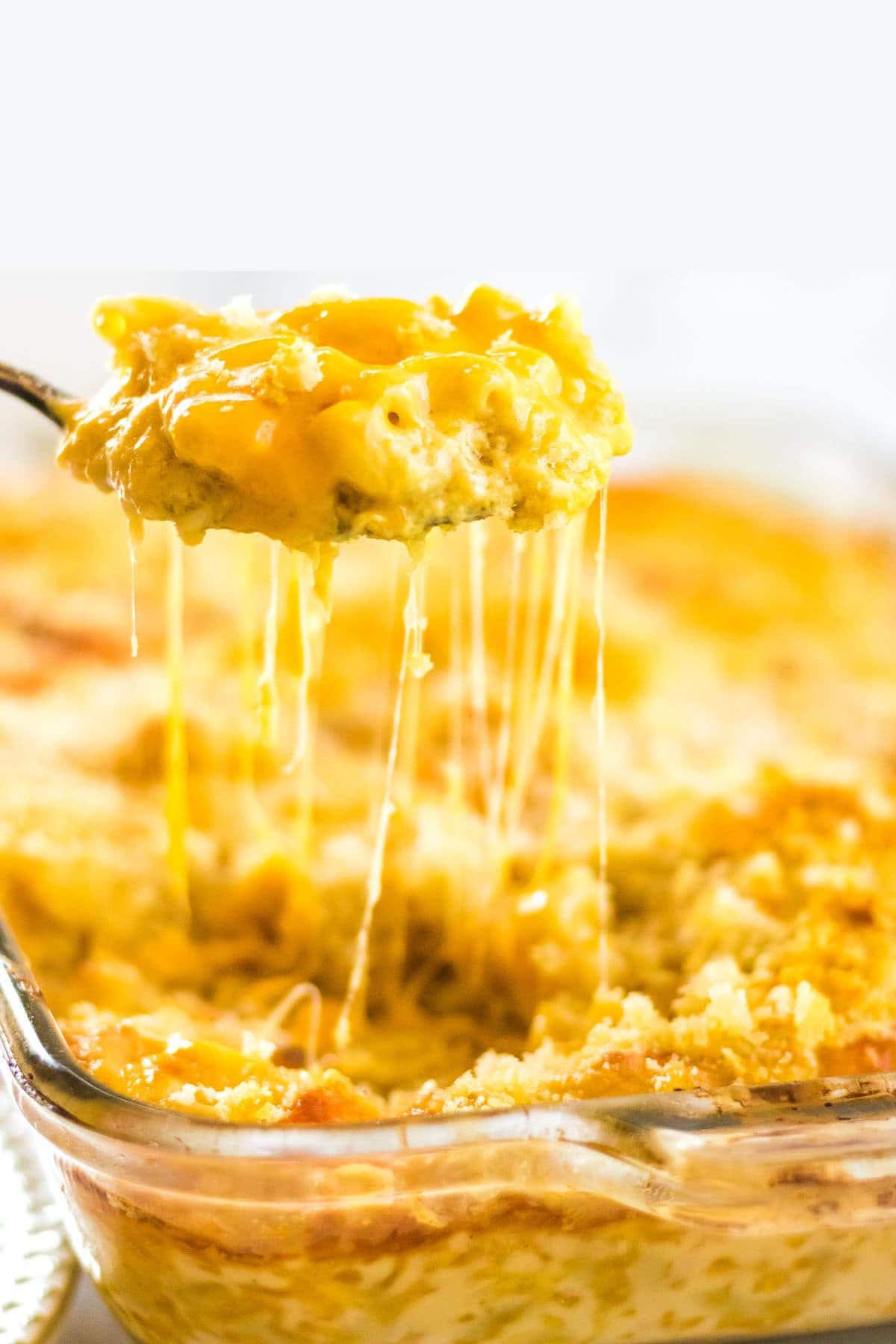 A serving of macaroni and cheese being lifted from the baking dish with melted strings of cheese hanging off the spoon.