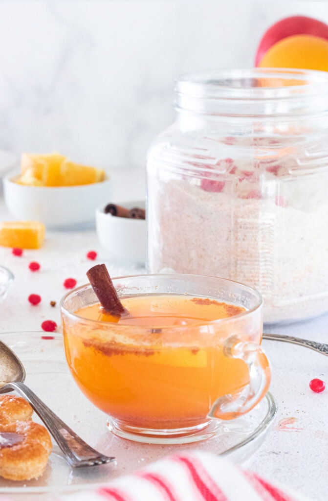 A cup of orange tea in front of a jar of mix.