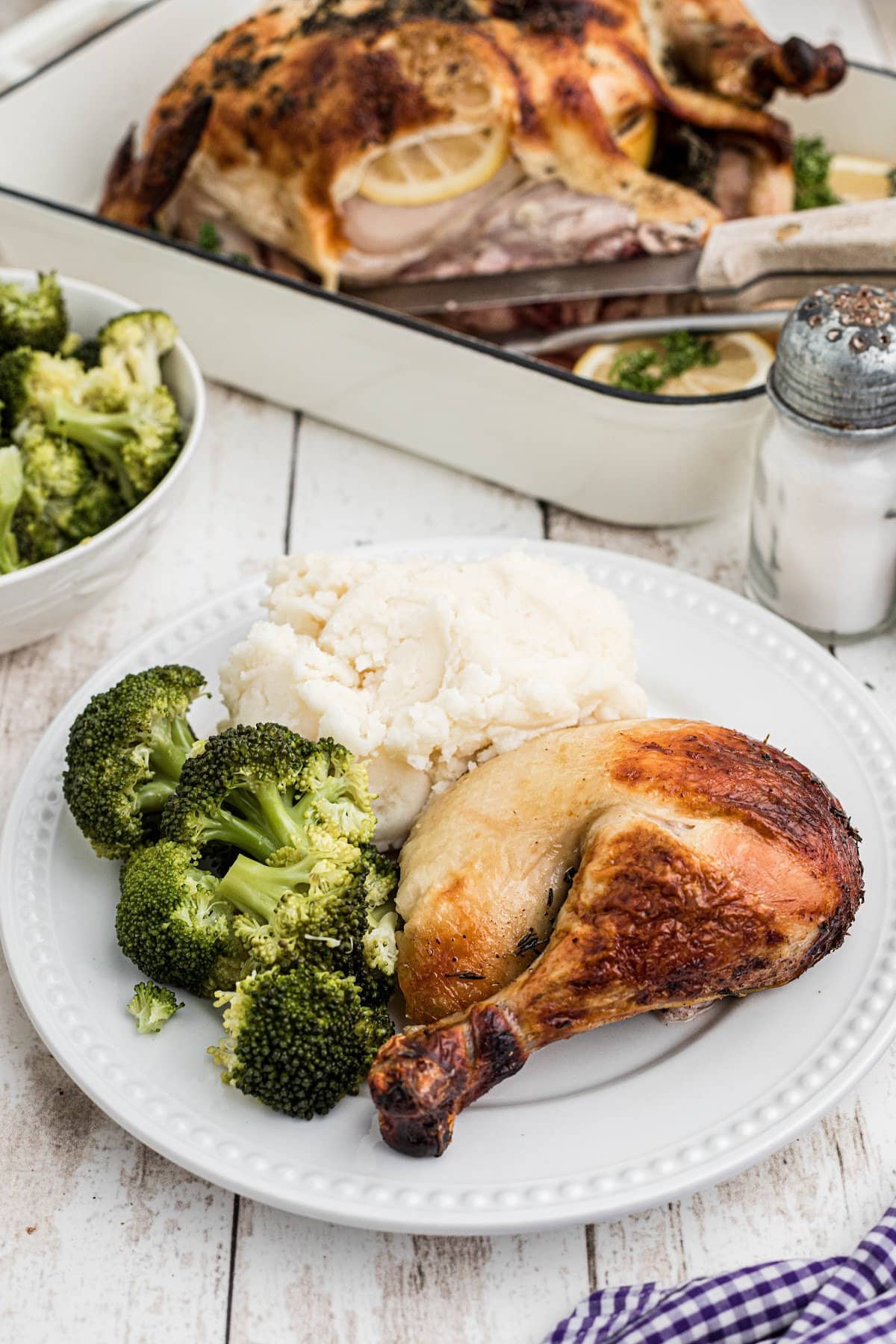 A serving of roast chicken on a white plate with broccoli and mash potatoes