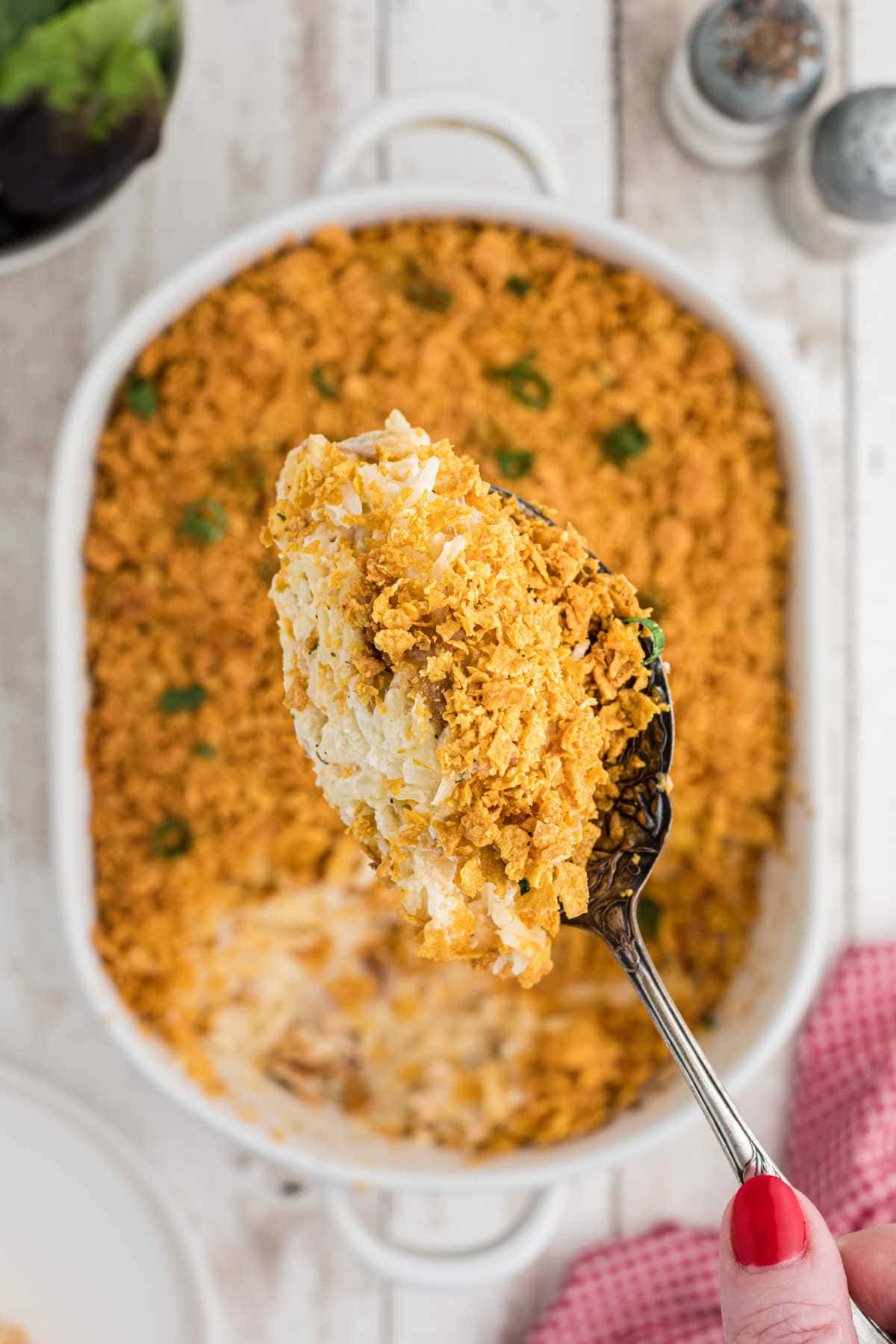 A spoonful of chicken hash brown casserole is shown close for texture
above a white casserole dish filled with the same.