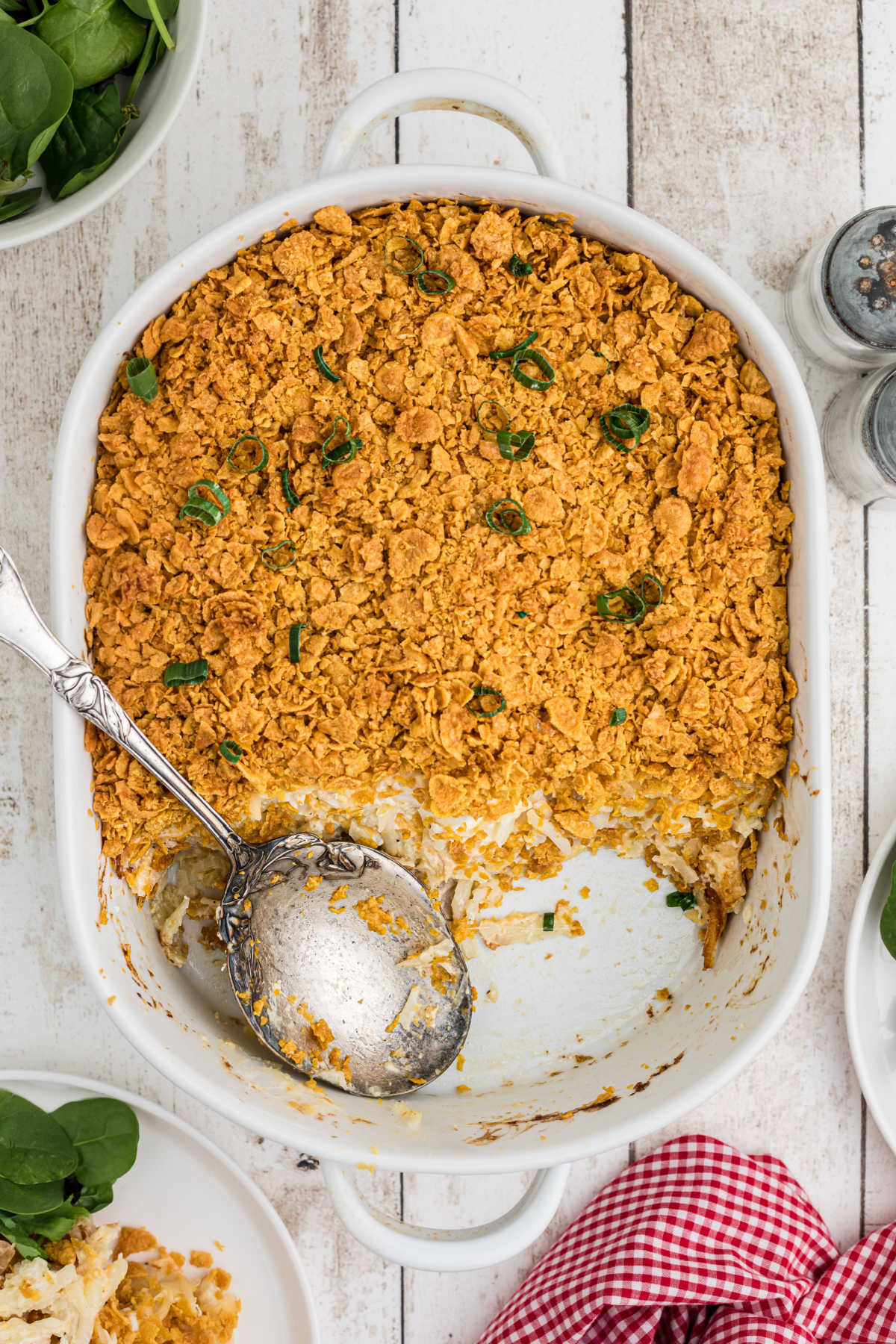 Chicken hash brown casserole baked in a white casserole dish shows a serving spoon and a healthy serving removed. 