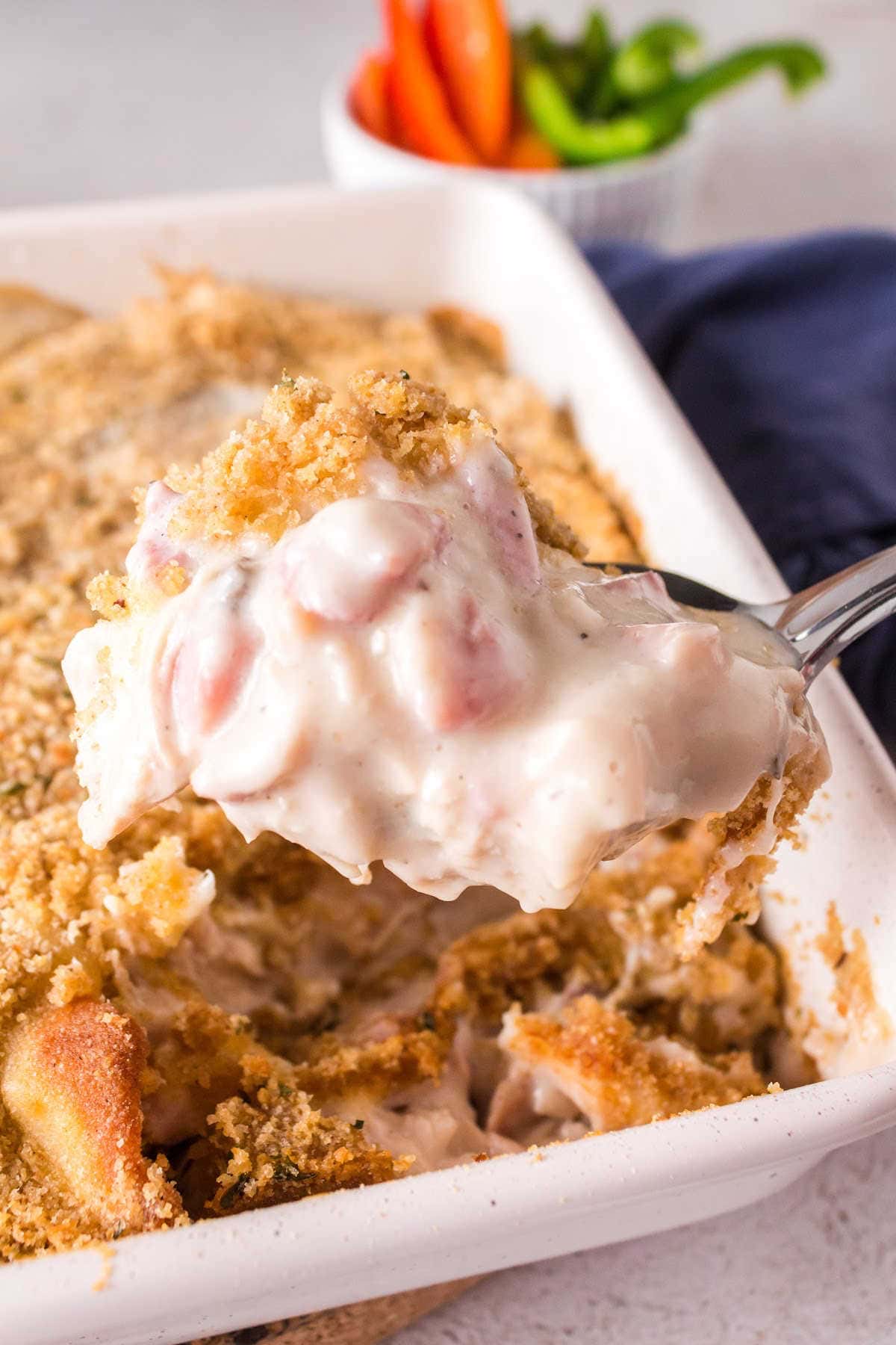 A forkful of cordon bleu casserole scooped out of a fresh casserole dish.