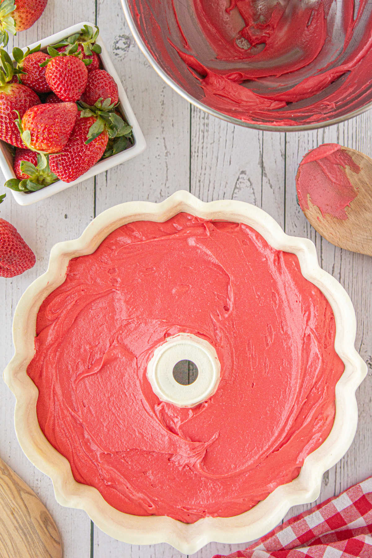 Strawberry bundt cake dough in bundt pan prior to cooking, along side mixing bowl and strawberries.