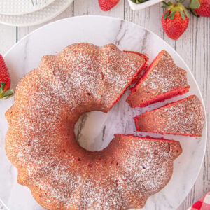 A marble plate displays a strawberry bundt cake with 2 slices cut to show the red cake color.