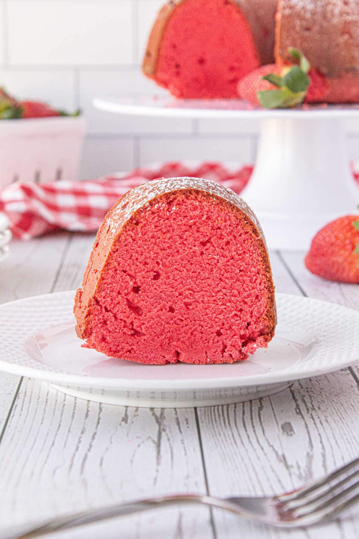 A slice on strawberry bundt cake on a white plate showing the beautiful red coloring of the cake.