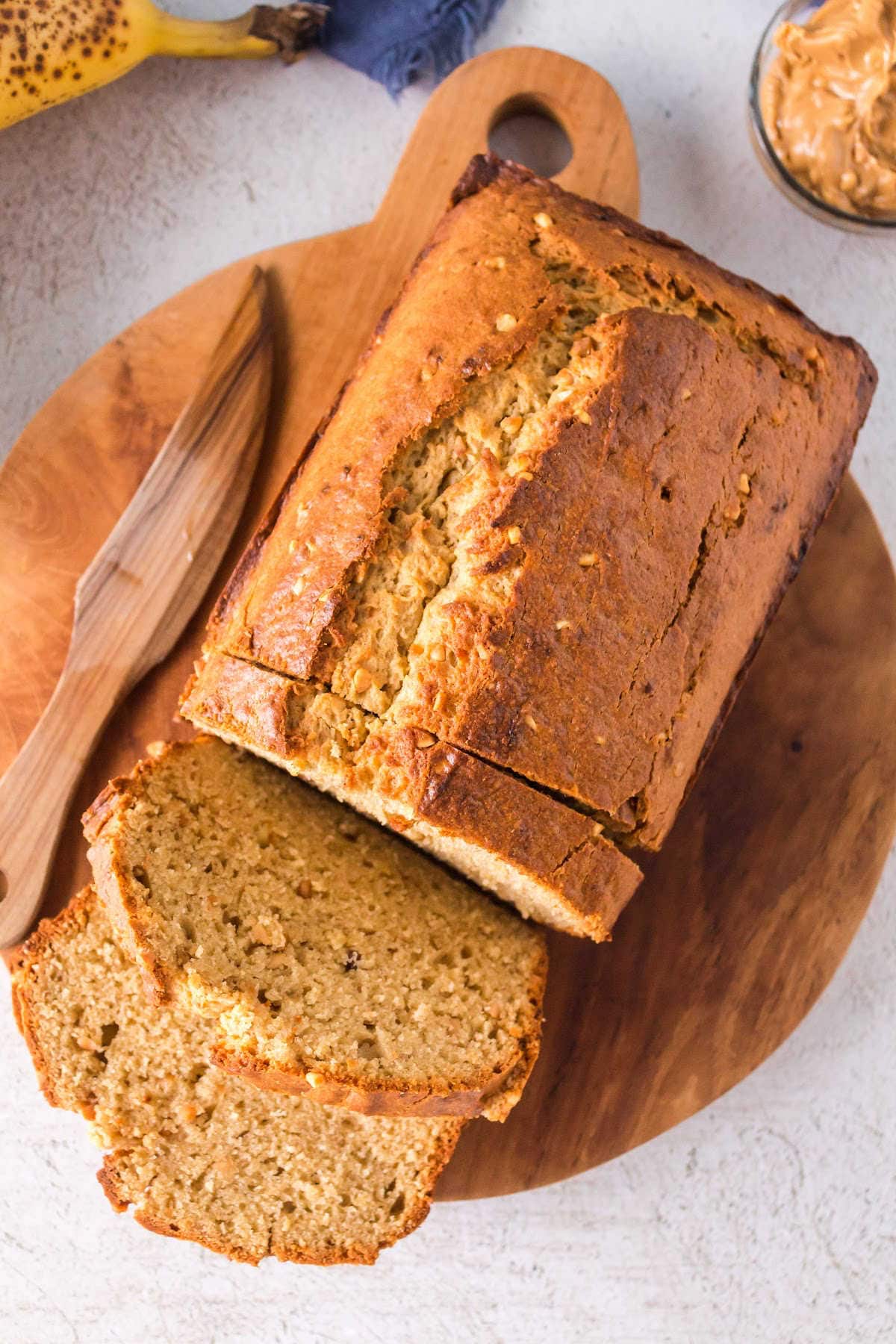 A sliced loaf of peanut butter banana bread on a wooden serving tray with a wooden knife placed beside it.