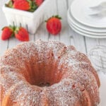 In the background is sliced strawberry bundt cake and strawberries; a cake server shows a cut slice of cake, and there is Pin text at the top.