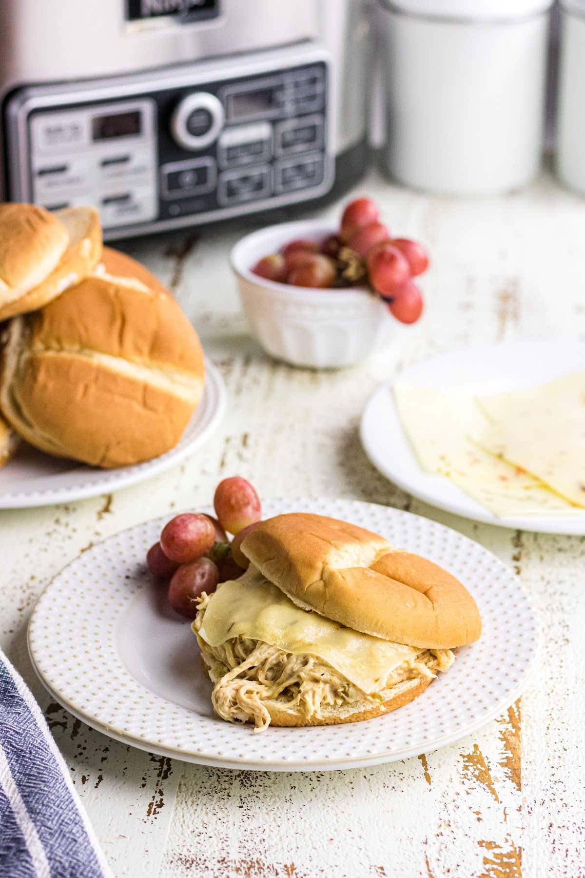 Slow Cooker Creamy Ranch Chicken Sandwich on a clean white plate with a side of purple grapes.