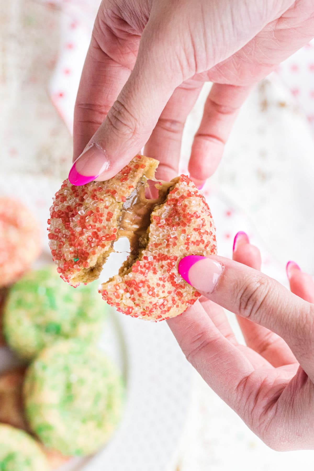 A warm cookie being broken in half showing the gooey caramel inside.