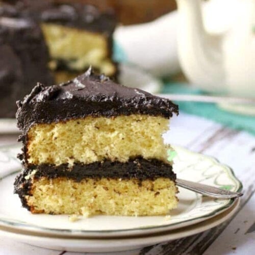 A slice of yellow layer cake with chocolate fudge frosting on a white plate.