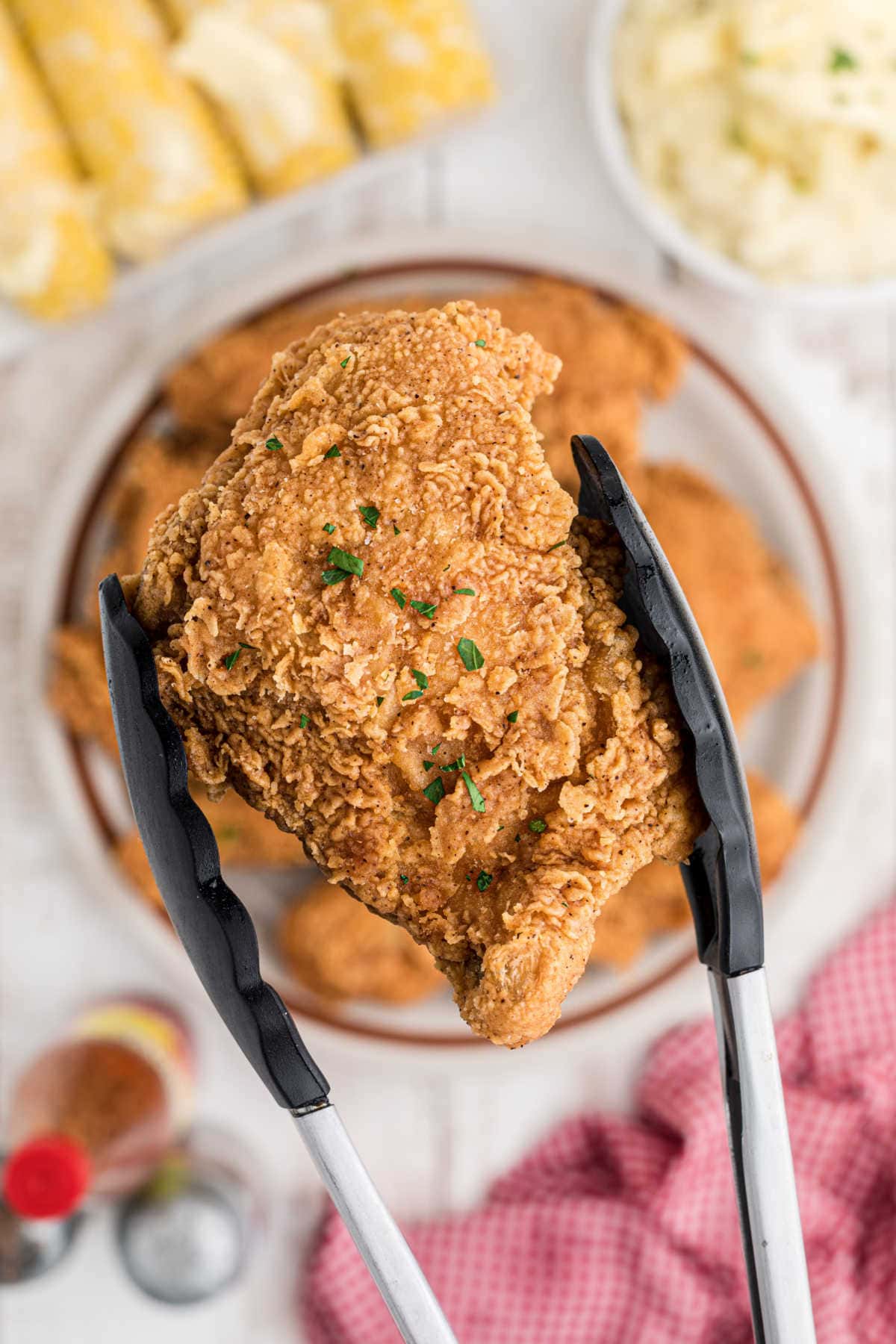 A piece of fried chicken being picked up with tongs.