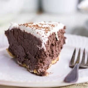Slice of chocolate silk pie with rich cocoa filling, whipped cream topping, and chocolate shavings on a crumb crust