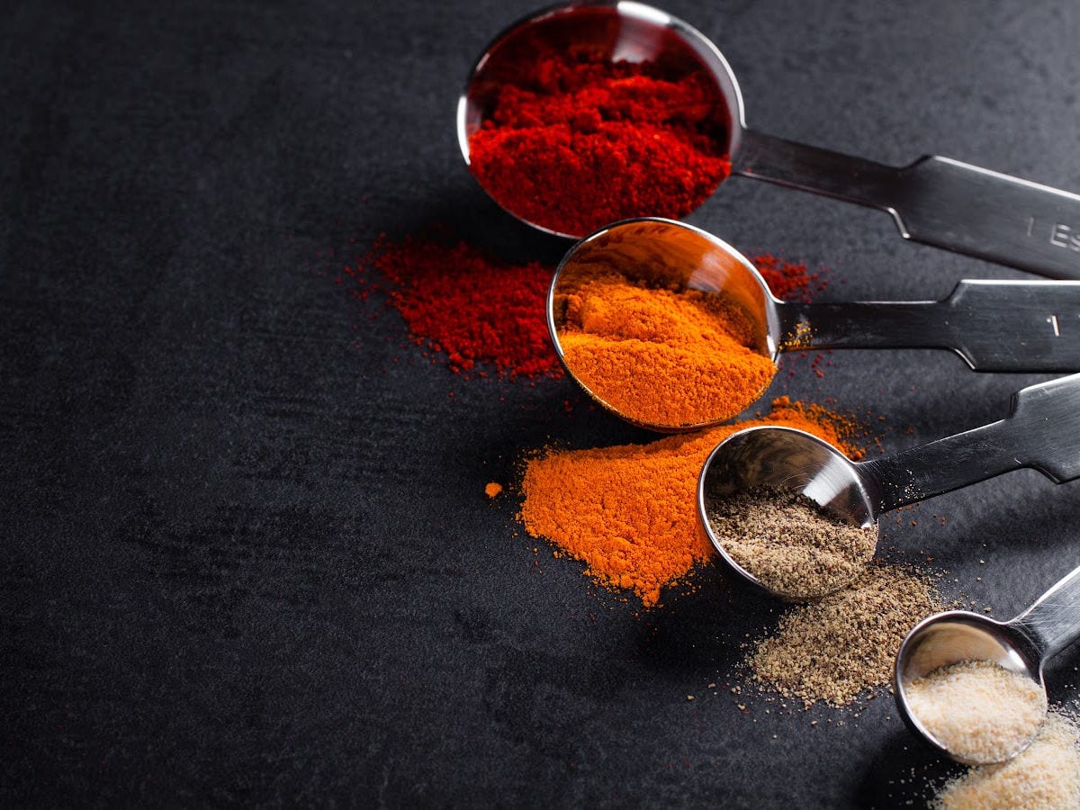 Measuring spoons filled with spices on a dark table.