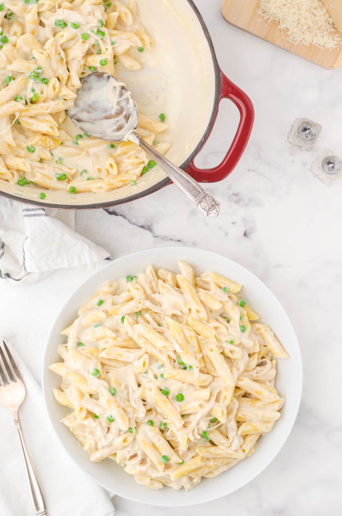 Overhead view of a pan of finished chicken alfredo with a full bowl nearby ready to be eaten.