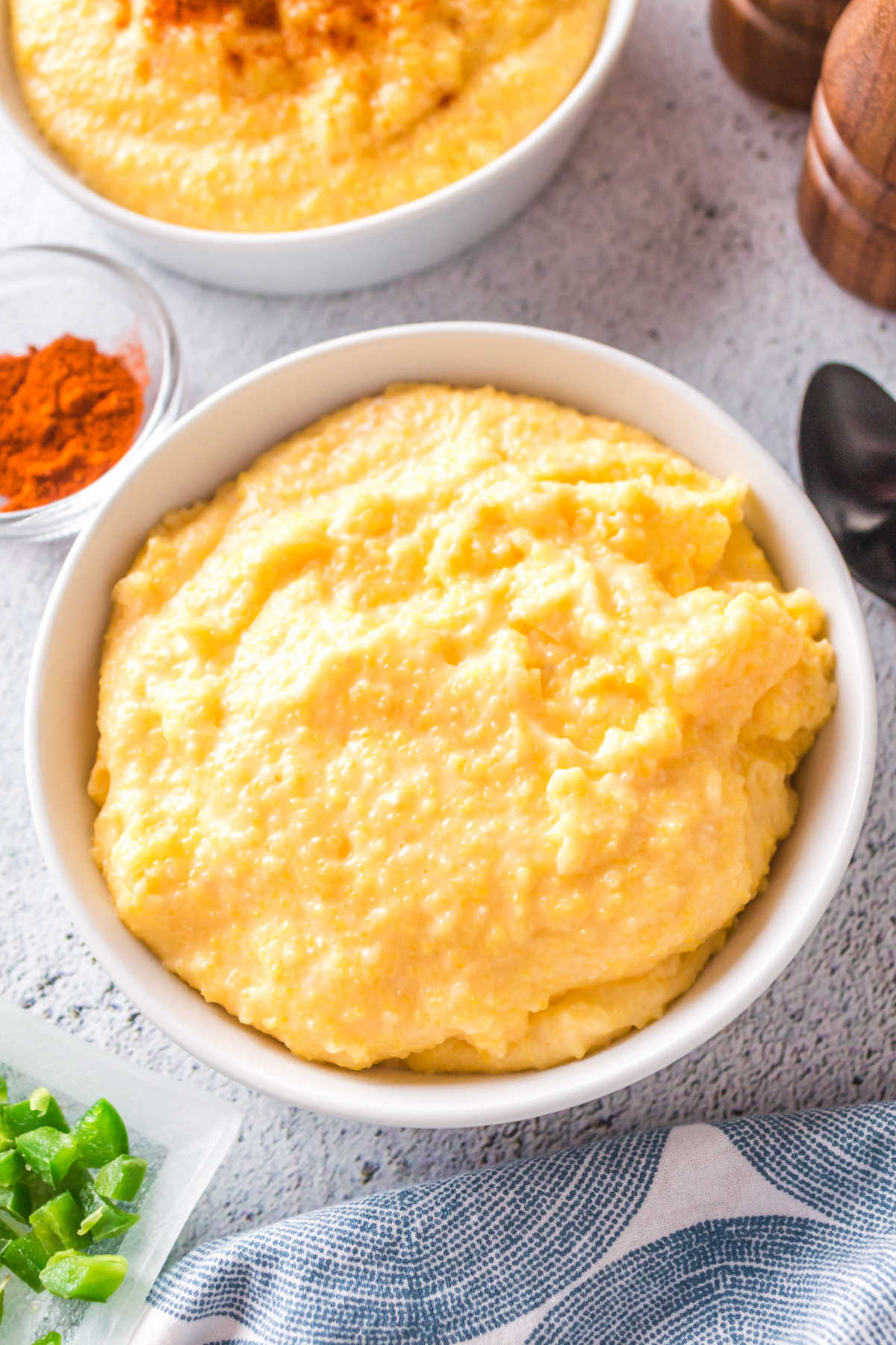 Overhead view of two bowls of cheese grits being garnished with paprika.